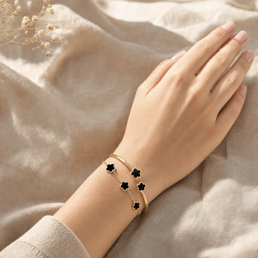 Black clover bracelet and open bangle worn stacked on wrist, gold finish